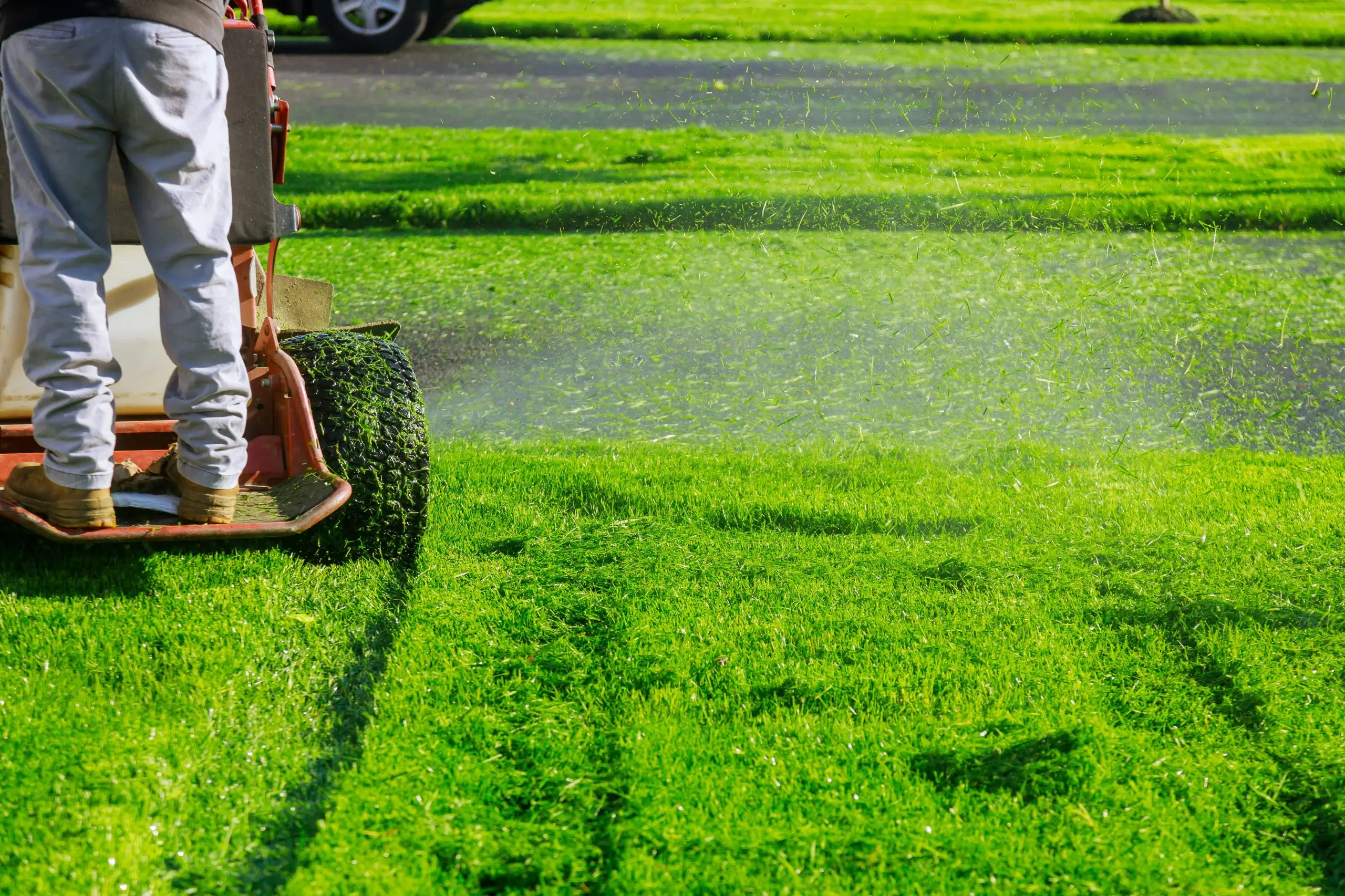 A wide-deck mower cutting a bright green lawn, throwing a spray of clippings